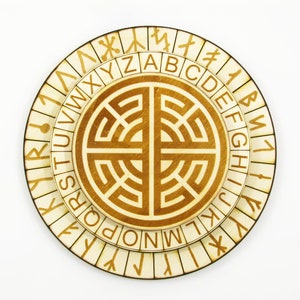 Puede incluir: Un disco de cifrado circular de madera con dos anillos giratorios. El anillo exterior presenta el alfabeto en un patrón circular, mientras que el anillo interior muestra una serie de símbolos. El centro del disco presenta un diseño decorativo.