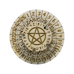 Può includere: Una ruota di cifratura circolare in legno con una stella a cinque punte al centro. La ruota ha più livelli con numeri, lettere e rune.