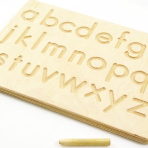 Peut inclure: Planche de tra&ccedil;age de l'alphabet en bois avec un stylet. La planche a les lettres de l'alphabet grav&eacute;es dessus, et le stylet peut &ecirc;tre utilis&eacute; pour tracer les lettres.