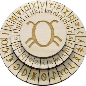 Può includere: Una ruota cifrata in legno con tre strati rotanti. Gli strati sono incisi con lettere, simboli e rune di colore marrone chiaro. Il cerchio centrale presenta un simbolo stilizzato. La ruota è progettata per codificare e decodificare messaggi.