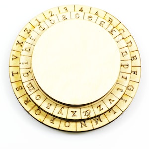 Può includere: Un disco di cifratura circolare in legno con più anelli concentrici di lettere e numeri. Il disco è in legno marrone chiaro e ha un centro vuoto.