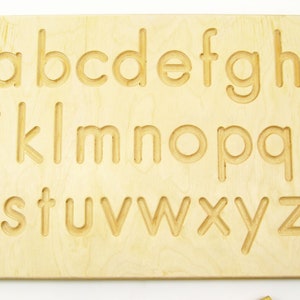 Peut inclure: Planche de tra&ccedil;age en bois de l'alphabet avec les lettres de a &agrave; z grav&eacute;es &agrave; la surface. La planche est de couleur brun clair et a une finition lisse.