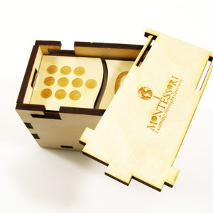 May include: A wooden box with a lid that opens to reveal a set of wooden circles. The box is labeled "MONTESSORI Learning through self discovery".