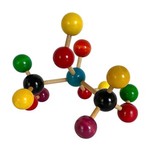 May include: A molecular model kit constructed from wooden sticks and multi-colored spheres. The spheres are painted in yellow, red, green, black, blue, and purple. The structure features a central core with various branches extending outward, creating a complex three-dimensional geometric arrangement of connected components.