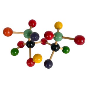May include: A molecular model kit featuring multicolored wooden spheres connected by light-colored wooden dowels. The spheres are painted in red, green, black, yellow, orange, and dark blue, representing atoms linked together in a complex structure.