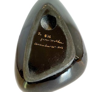 May include: A black, triangular-shaped object with a glossy finish. The underside features a circular opening and handwritten text in gold ink that reads "To Bill from Mother December 25, 1956."