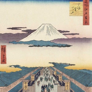 May include: Japanese woodblock print depicting a bustling street scene with Mount Fuji in the background. The print features a long street lined with buildings, filled with people. The sky transitions from blue to a soft pink, with the snow-capped mountain in the distance.