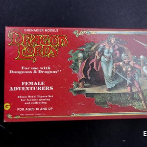 Puede incluir: Una caja roja para Dragon Lords de Grenadier Models, con una ilustración de fantasía de aventureras. La caja incluye el texto "Para usar con Dungeons & Dragons" y "Female Adventurers". La caja es para mayores de 10 años.