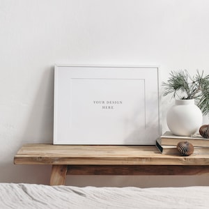 Peut inclure: Un cadre photo blanc avec un passe-partout blanc et le texte "YOUR DESIGN HERE" sur une table en bois avec un vase blanc contenant des branches vertes et des ornements marrons.