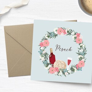 May include: A blue card with a floral wreath surrounding a bottle of wine, a glass of wine, and a piece of matzah. The text "Pesach" is written in the center of the card.
