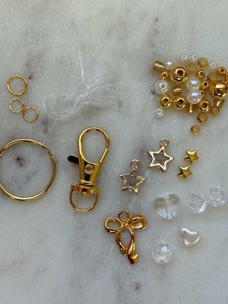 May include: A kit for making a charm bracelet with gold-toned charms, beads, and a clasp. The kit includes a variety of charms, including stars, hearts, and a bow. The beads are a mix of gold and white.
