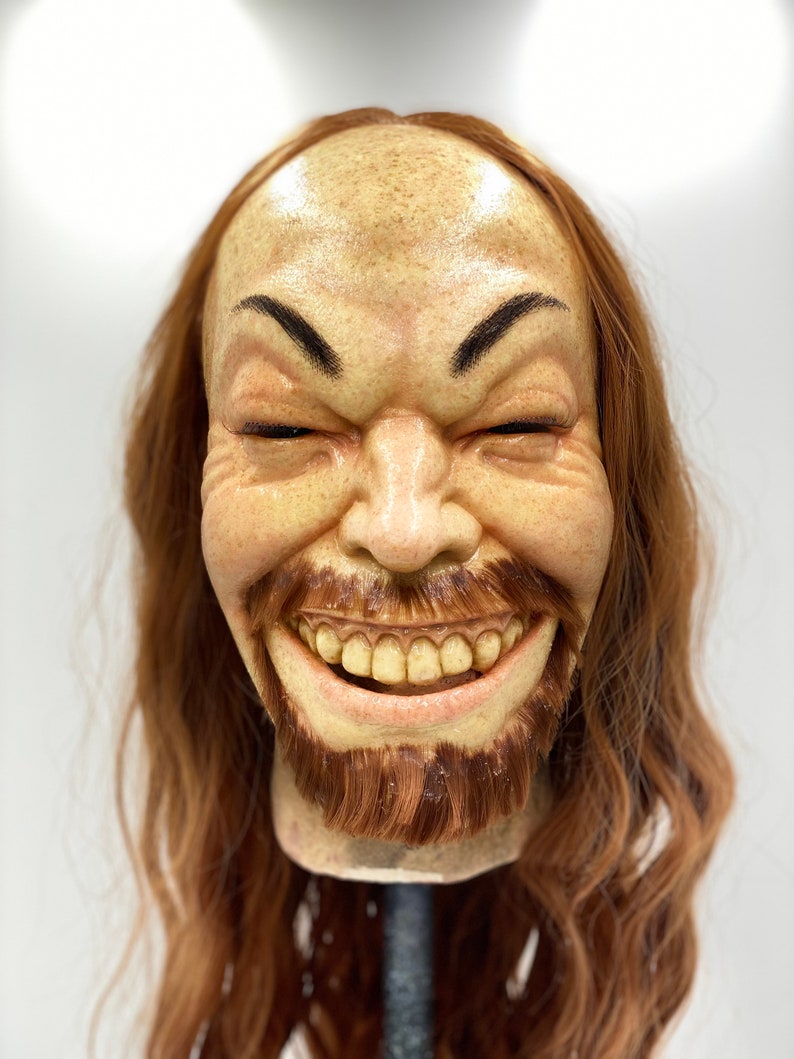 May include: A realistic-looking, hand-crafted, human head sculpture with a long, brown wig. The sculpture has a wide smile with visible teeth and a brown beard.