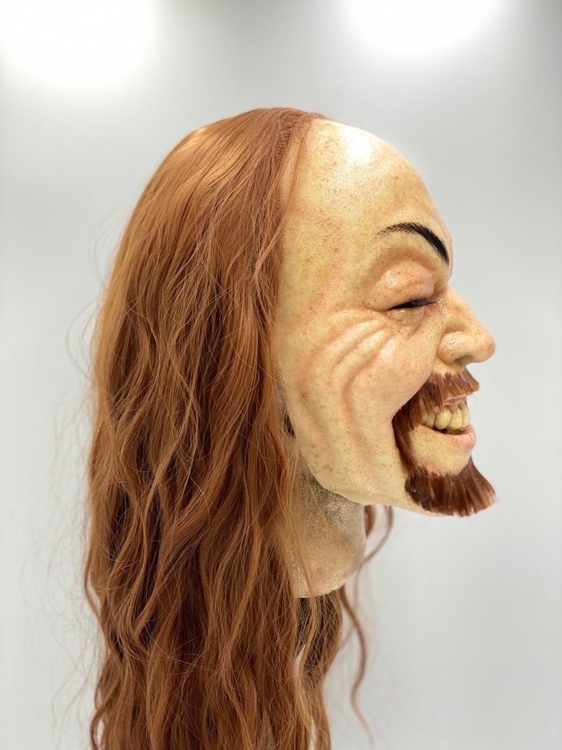 May include: A realistic-looking, hand-painted, sculpted mask of a man with long, wavy, auburn hair and a beard. The mask is smiling with a mischievous expression.