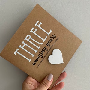 May include: A brown card with the text "THREE amazing years" and the words "Happy Anniversary to my wonderful husband". A white heart is attached to the card.