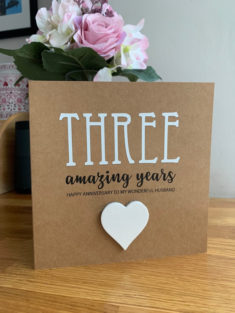 May include: A brown card with the text "THREE amazing years" and "HAPPY ANNIVERSARY TO MY WONDERFUL HUSBAND". A white heart is attached to the card.