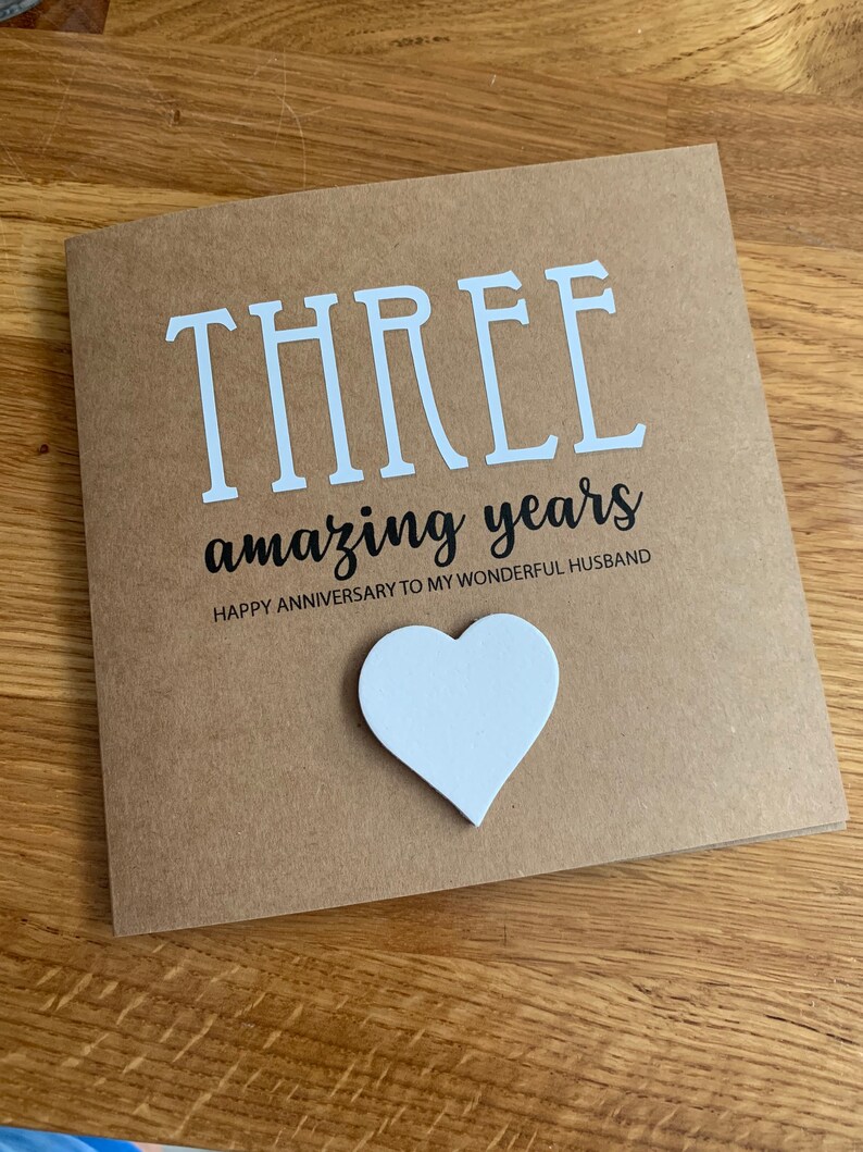 May include: A brown card with the text "THREE amazing years" and "HAPPY ANNIVERSARY TO MY WONDERFUL HUSBAND". A white heart is attached to the card.