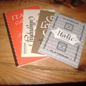 May include: A collection of four instructional booklets on calligraphy. The books feature various cover designs in orange, cream, brown, and gray, with printed text including Italic, Calligraphy, Sheaffer, and Platignum.