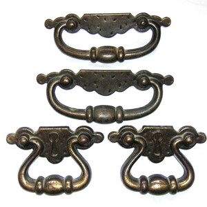 May include: Four antique brass cabinet pulls with ornate designs. Two pulls have a keyhole and two pulls have a simple, rounded design.