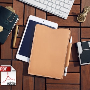 May include: A light tan leather tablet case with a white stylus in a side pocket. The case is on a wooden surface with a white keyboard, a black notebook, and a gold pen. A PDF icon is in the lower left corner.
