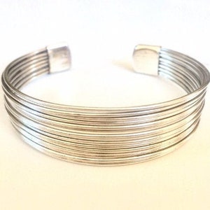May include: A silver bangle bracelet made of multiple thin, stacked bands.