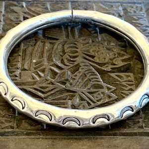 Può includere: Un braccialetto in argento con un design a forma di luna crescente. Il braccialetto è liscio e lucido.