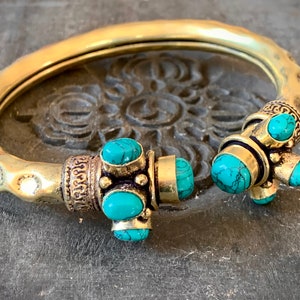 May include: A gold bangle bracelet with turquoise stones. The bracelet is decorated with intricate details and has a hammered finish.