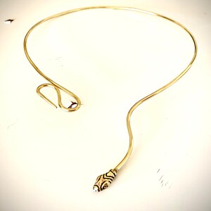 May include: A gold-toned choker necklace with a snake head design at the end. The necklace is made of a thin, flexible wire.
