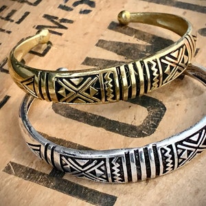 Può includere: Due semplici braccialetti a forma di bangle con un motivo geometrico. Il braccialetto in alto è dorato con un motivo nero. Il braccialetto in basso è argentato con un motivo nero.