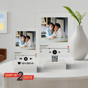 May include: Two clear acrylic photo frames with a music player design. Each frame features a photo of two women and the song title "Stand By You" by Rachel Platten. The frames have a play button, a pause button, a skip forward button, a skip back button, and a volume control.