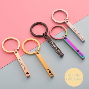 May include: Set of five personalised bar keychain charms with different engraved messages. The charms are in various colours, including gold, silver, black, and rainbow. The messages include "I Love You", "JOP 08/18/23", "Drive Safe We Need You Here", and "Andie Frank Thank You For Coming 2024".