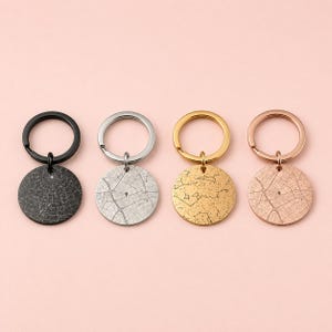 May include: Four circular keychains with split rings, each featuring a unique engraved design. The set includes a black keychain with a star map, a silver keychain with a city street map, a gold keychain with a constellation, and a rose gold keychain with a city street map.