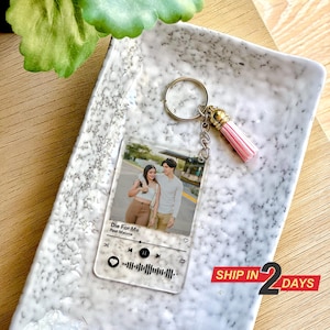 May include: A clear acrylic keychain featuring a photo of a couple and a Spotify music player design. The music player displays the song "Die For Me" by Post Malone. The keychain has a pink tassel.