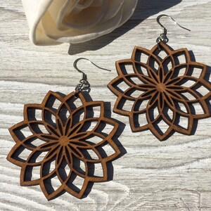 K&ouml;nnte beinhalten: Ein Paar Holzohrringe mit einem Mandala-Design. Die Ohrringe sind braun und haben ein zartes, filigranes Muster. Sie h&auml;ngen an silbernen Haken.
