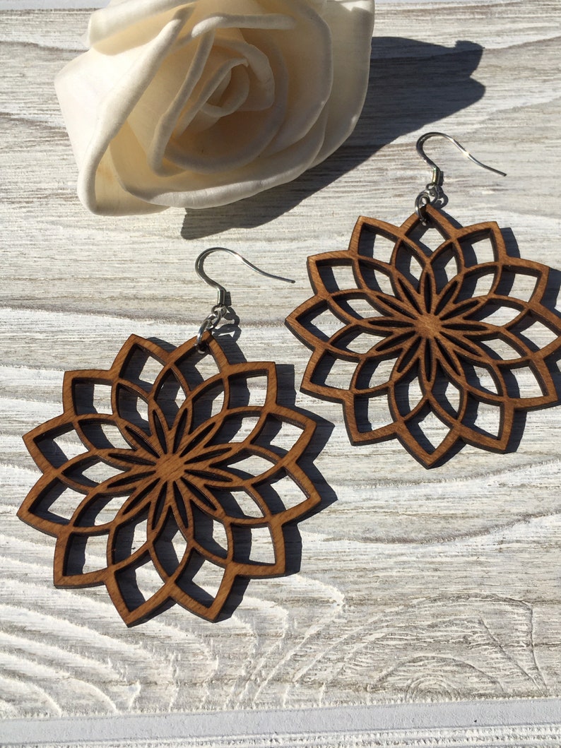 K&ouml;nnte beinhalten: Ein Paar Holzohrringe mit einem Mandala-Design. Die Ohrringe sind braun und haben ein zartes, filigranes Muster. Sie h&auml;ngen an silbernen Haken.
