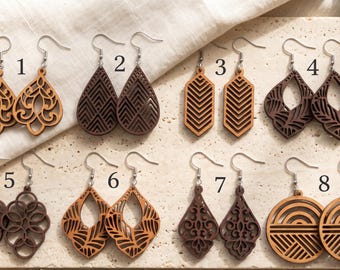 May include: Eight pairs of laser-cut wooden earrings with silver-toned metal hooks, numbered one through eight. The designs feature various geometric, floral, and circular patterns in light and dark brown wood tones, arranged in two rows.