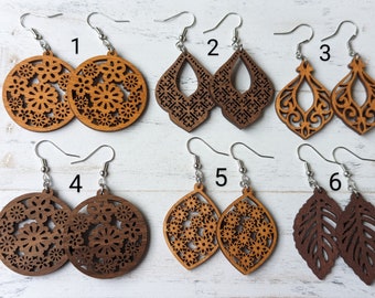 May include: Six pairs of laser-cut wooden earrings with silver-toned metal hooks, numbered one through six. The designs include circular floral patterns, teardrop shapes with intricate cutouts, and leaf silhouettes in light and dark wood tones.
