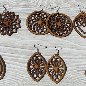 K&ouml;nnte beinhalten: Sechs Paar Holzohrringe mit filigranen Laser-Schnitten. Die Ohrringe haben verschiedene Formen, darunter Kreise, Ovale und Dreiecke. Die Designs zeigen geometrische Muster und florale Motive. Die Ohrringe sind braun und haben silberne Haken.