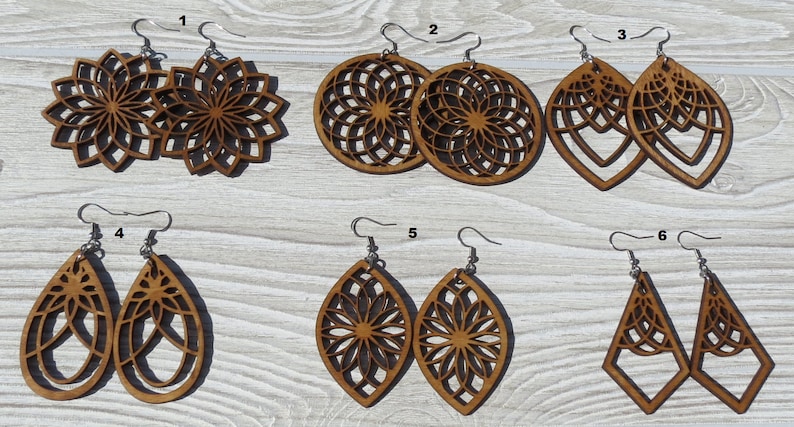 K&ouml;nnte beinhalten: Sechs Paar Holzohrringe mit filigranen Laser-Schnitten. Die Ohrringe haben verschiedene Formen, darunter Kreise, Ovale und Dreiecke. Die Designs zeigen geometrische Muster und florale Motive. Die Ohrringe sind braun und haben silberne Haken.