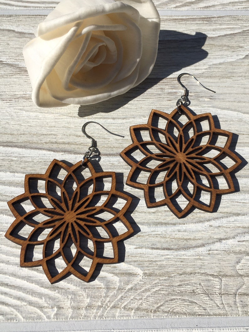K&ouml;nnte beinhalten: Ein Paar Holzohrringe mit einem geometrischen Mandala-Design. Die Ohrringe sind braun und haben ein zartes, filigranes Muster. Sie h&auml;ngen an silbernen Haken.