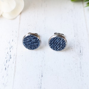 May include: A pair of silver stud earrings with a round denim fabric design.