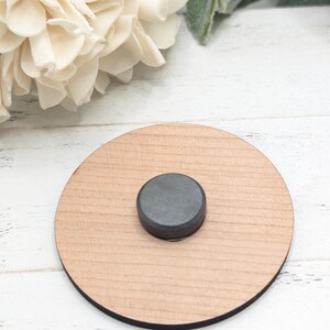 Pu&ograve; includere: Un sottobicchiere rotondo in legno con un magnete nero al centro.