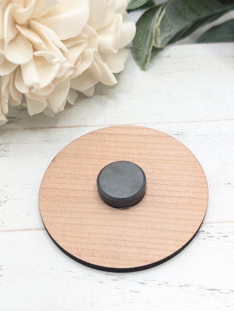 Pu&ograve; includere: Un sottobicchiere rotondo in legno con un magnete nero al centro.