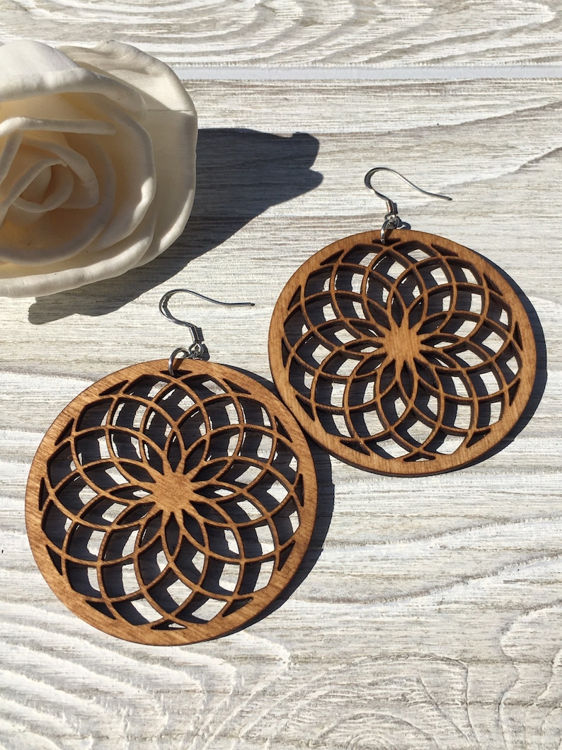 K&ouml;nnte beinhalten: Ein Paar Holzohrringe mit einem runden Design mit einem geometrischen Muster. Die Ohrringe sind braun und haben silberne Haken.