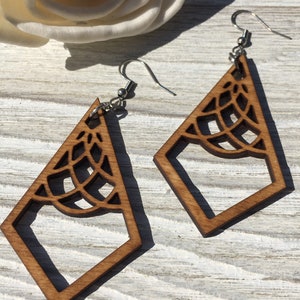 K&ouml;nnte beinhalten: Ein Paar Holzohrringe mit geometrischem Design. Die Ohrringe sind braun und haben ein zartes, filigranes Muster. Sie h&auml;ngen an silbernen Haken.
