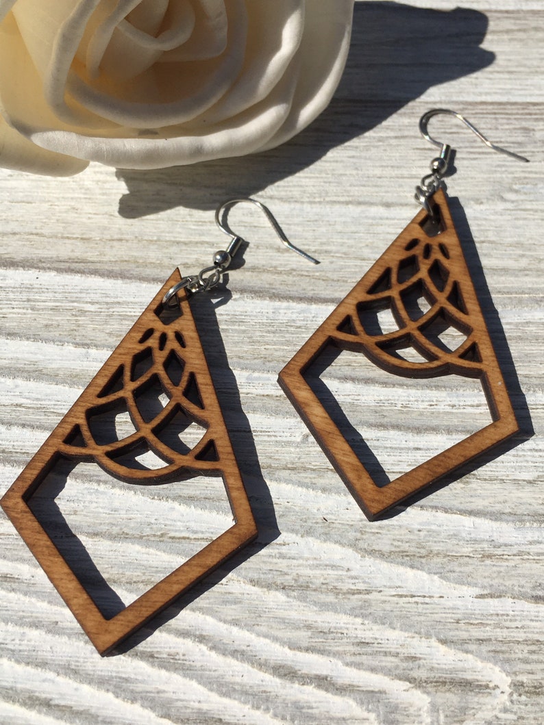 K&ouml;nnte beinhalten: Ein Paar Holzohrringe mit geometrischem Design. Die Ohrringe sind braun und haben ein zartes, filigranes Muster. Sie h&auml;ngen an silbernen Haken.