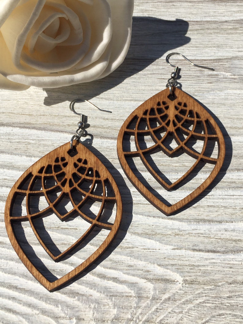 K&ouml;nnte beinhalten: Ein Paar braune Holzohrringe mit geometrischem Design. Die Ohrringe sind tropfenf&ouml;rmig und haben ein filigranes, kompliziertes Muster.