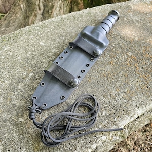 Op de afbeelding: Zwarte leren mes schede met een zwarte paracord lanyard. De schede heeft een drukknoop sluiting en meerdere rijen stiksels.