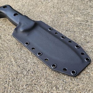 Puede incluir: Funda de cuchillo de cuero negro con múltiples ojales alrededor del perímetro. La funda está diseñada para sujetar un cuchillo con mango negro.