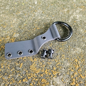 May include: A gray leather belt loop with three metal eyelets and a black metal D-ring. Two black metal screws are included.