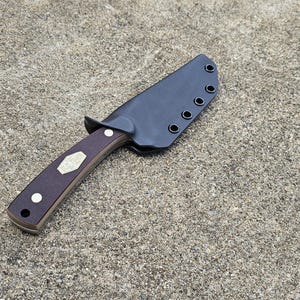 May include: A knife with a brown handle and a black leather sheath. The sheath has five stitching holes.